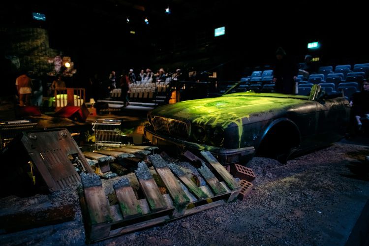 Empty set of the Angel Esmeralda, with detritus and a ruined car spray painted green and yellow